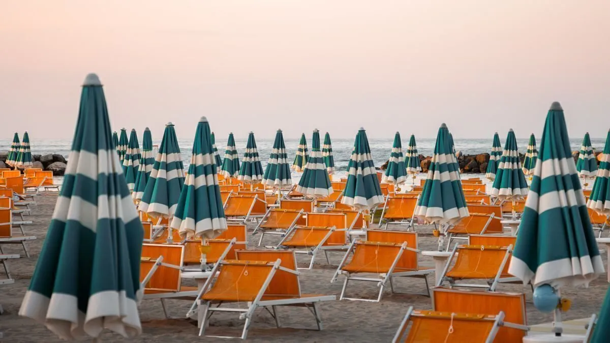 File di ombrelloni verdi e bianchi chiusi con i lettini arancioni allineati, alla luce dell'alba