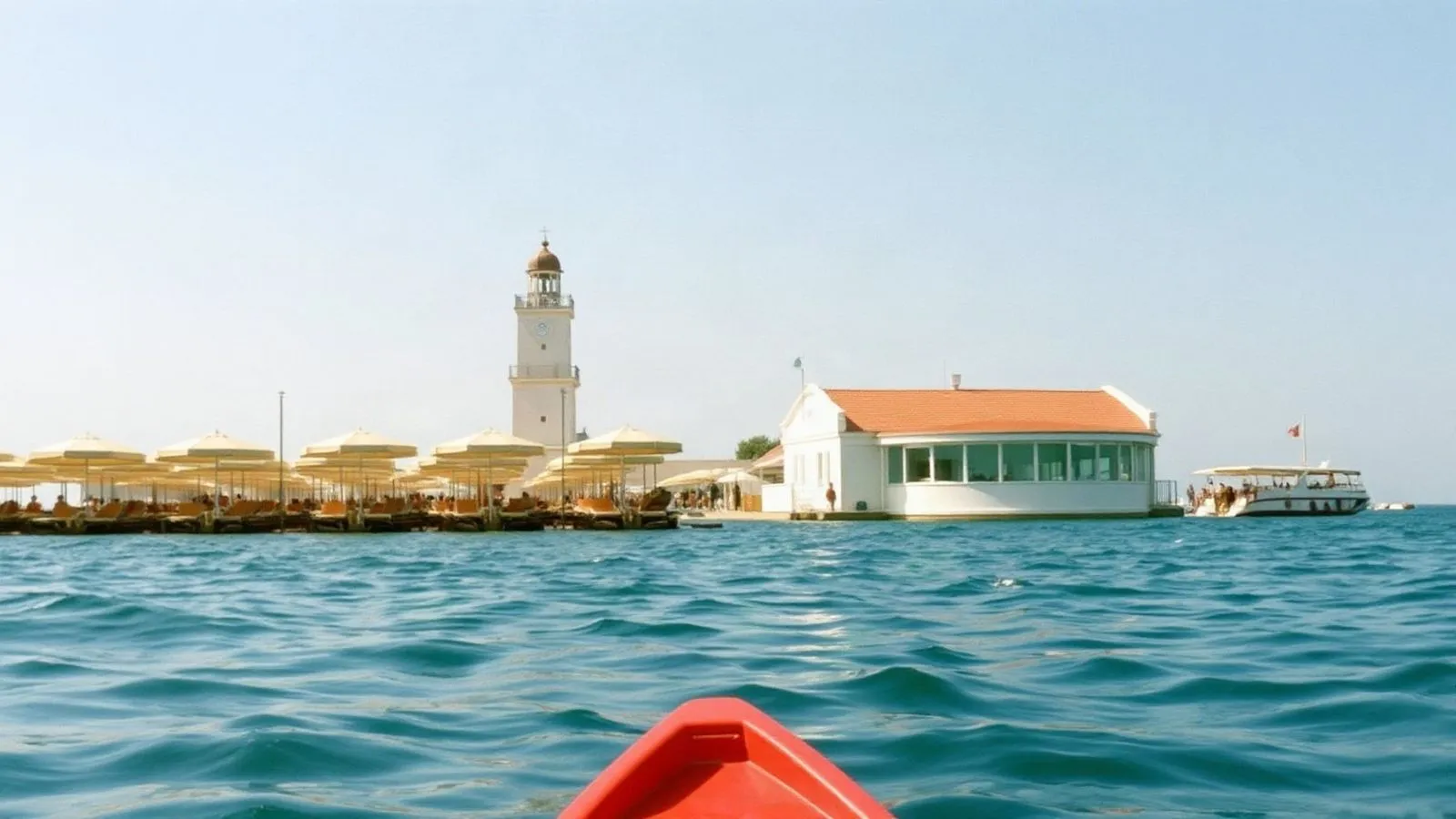 Stabilimento balneare su palafitta visto dall'acqua, con le file di lettini sotto le tettoie e la torretta con l'orologio