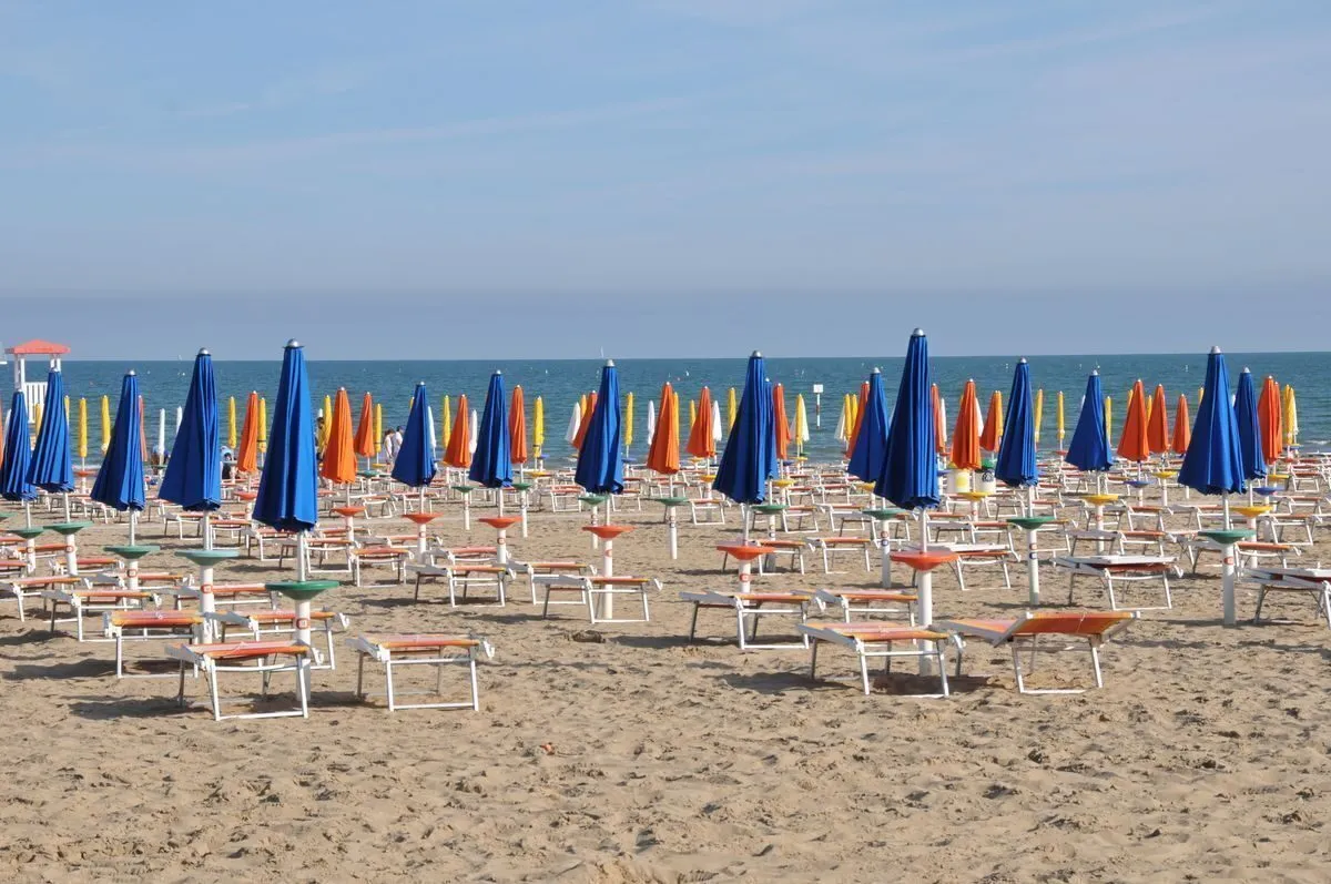 File fitte di ombrelloni chiusi blu e arancioni su una lunga spiaggia adriatica