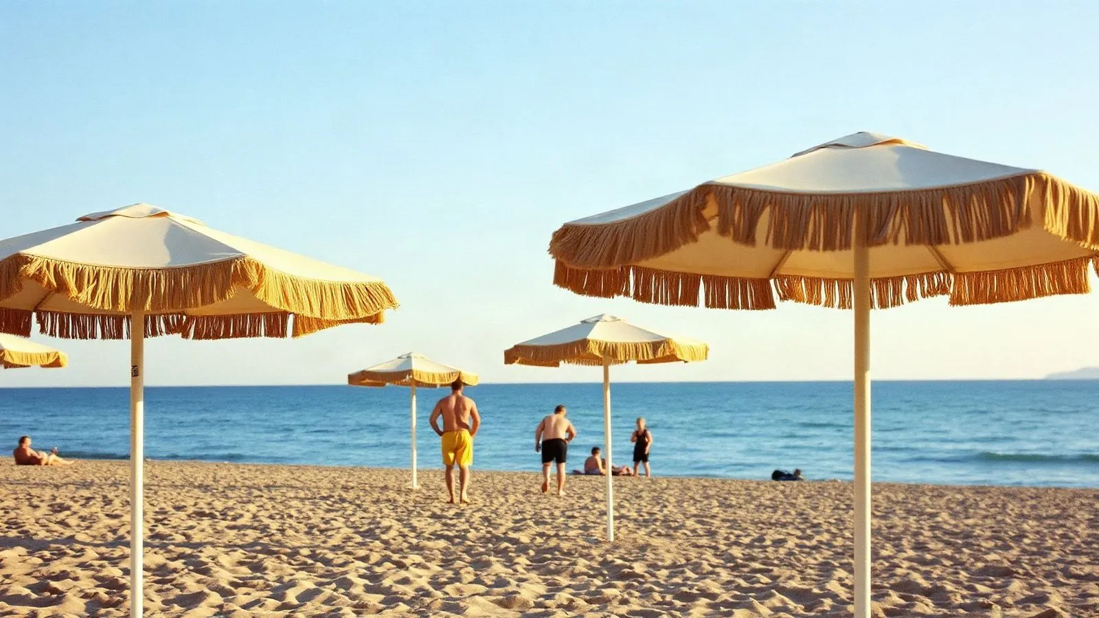 Spiaggia di settembre con ombrelloni aperti e poche persone sparse nella luce bassa del tardo pomeriggio