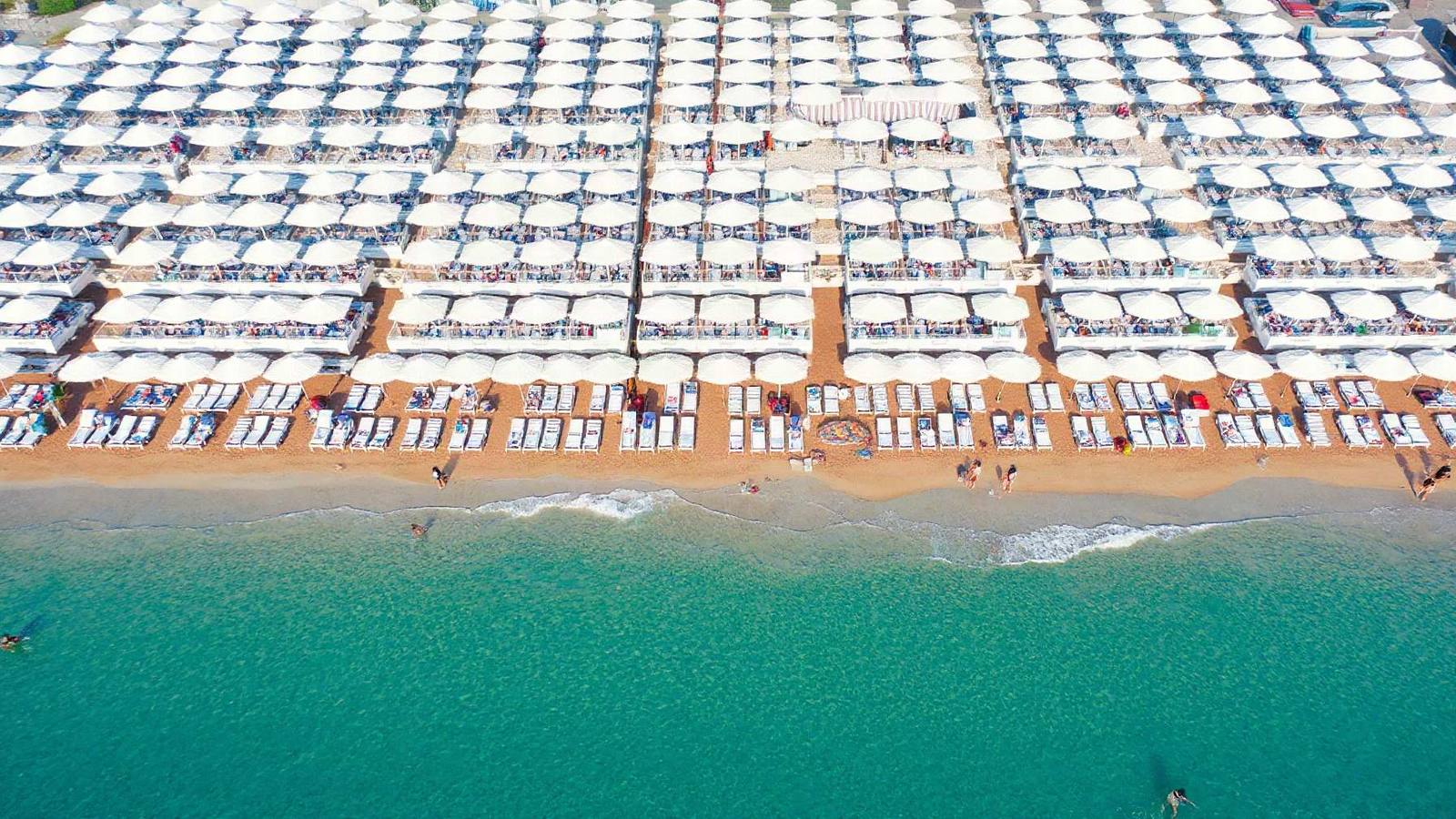 Stabilimento balneare ripreso dall'alto con le file di ombrelloni bianchi, i lettini e i bagnanti sulla battigia